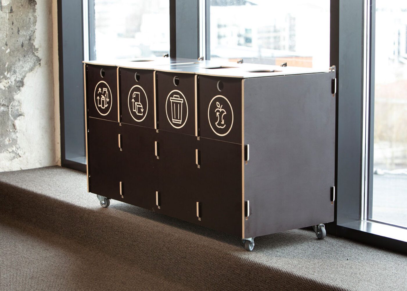 Recycling bins made of durable plywood with labeled sections for packaging, paper, mixed, and bio waste, placed in a modern office setting.