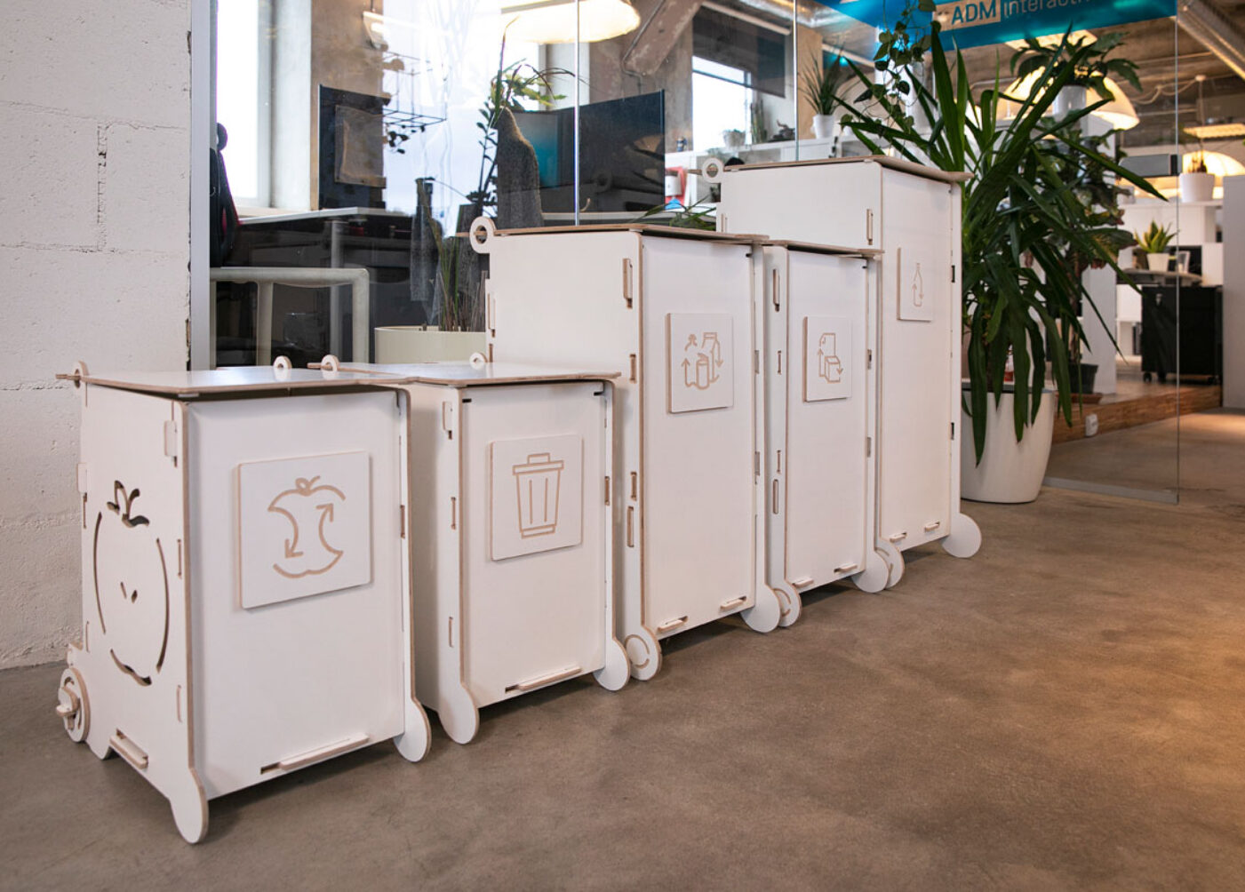 Modern white waste bins with lids and wheels, ideal for offices or public interiors, featuring separate sections for paper, packaging, and bio waste.